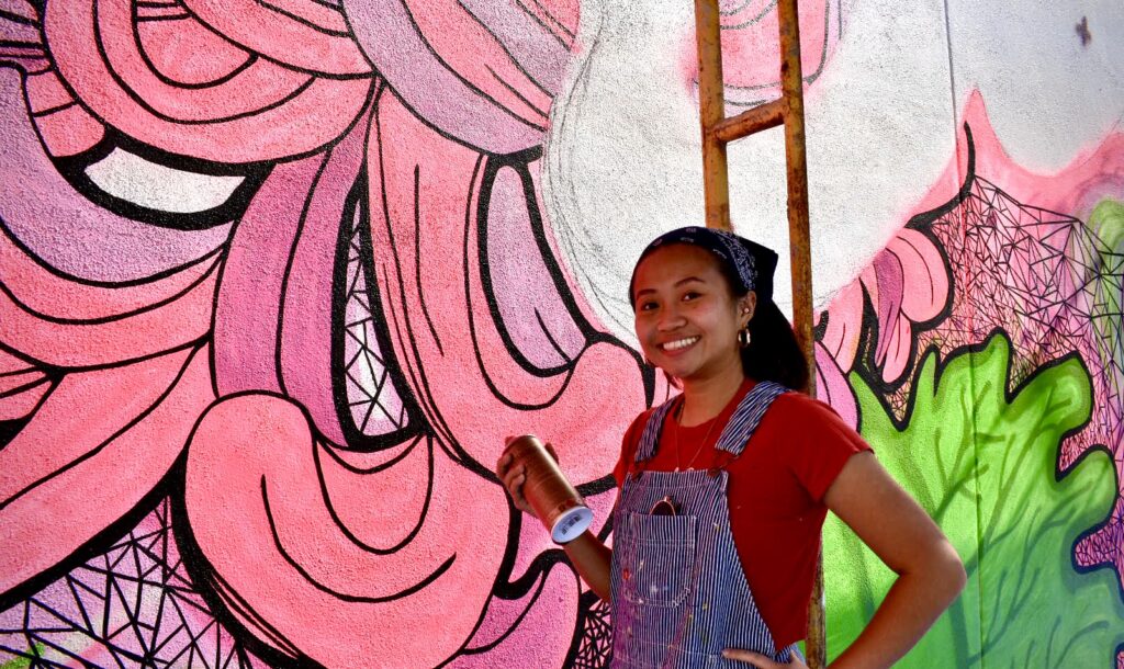 Annie Dong smiling next to her Red Crowned Cranes mural.