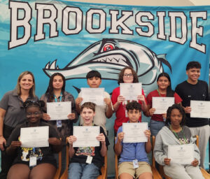 Middle school students pose holding certificates in front of a banner that reads "Brookside."