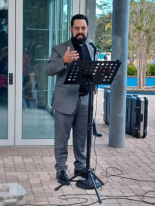 Alex Evangelista speaks into a microphone and addresses a crowd.