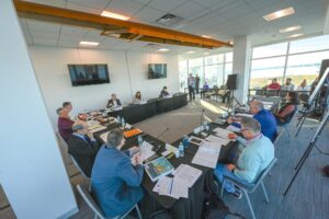 Sarasota County Commissioners and staff sit around tables in a conference room.