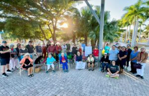 Rows of people stand outdoors and face the camera, some holding signs in support of immigrants.