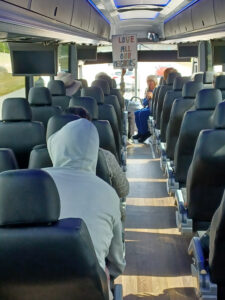 Interior of a half-full bus. Someone at the front holds up a sign that reads "Love all our neighbors".
