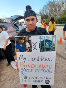 Roxana Torres holding a sign that reads, "My husband been detained since October 30. The children need their father".