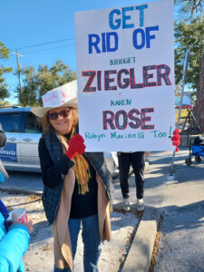 A demonstrator holding a sign that reads "Get rid of Bridget Ziegler + Karen Rose (Robyn Marinelli Too!)