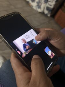 Hands holding a smartphone displaying a photo of a smiling person in a suit at a desk.