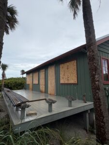 The damaged deck of a building with boarded-up windows.