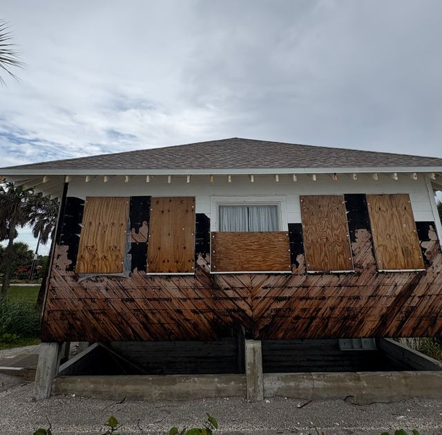 The damaged side of a building with boarded-up windows.