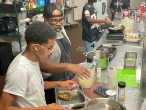 Chef G instructs a student in a kitchen.
