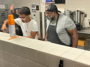 Chef G instructs a student in a kitchen.