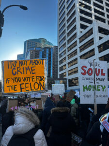 Demonstrators on a crowded city street hold anti-ICE and anti-Trump signs.
