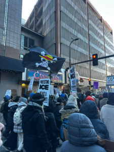 Demonstrators on a crowded city street hold anti-ICE signs.