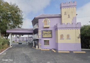 A pale purple and yellow motel building styled as a castle with a sign that reads "Magic Castle Inn & Suites."