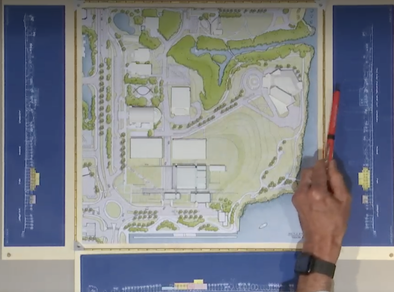 A person uses a writing utensil to gesture to a map of the proposed Bay Park area.