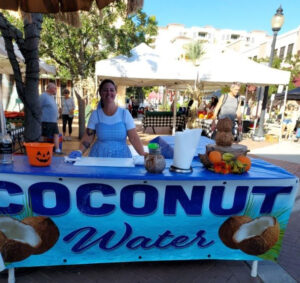 A smiling vendor at a market stall advertising coconut water.