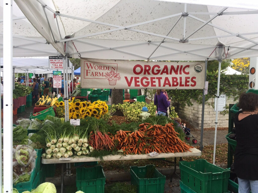 A market stall stoicked with fennel and carrots with a sign advertising Worden Farm's organic vegetables.