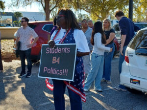A demonstrator in a crowd holds a sign that reads "Students B4 Politics!!!"