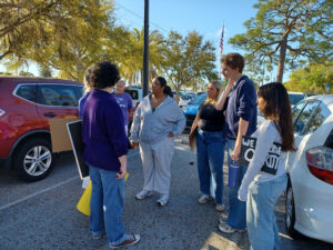 Demonstrators talk amongst themselves. One holds a sign tucked under their arm that appears to read "We deserve clarity".