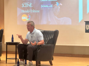 Urban Meyer pointing while speaking in a chair on stage.