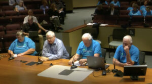 Four people sitting at a table in a meeting hall.