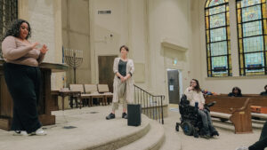 Jodany Del Rosario stands at the front of a church and gesticulates while speaking.