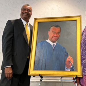 Charles Williams smiling with a painted portrait of himself.