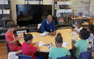 Jimmy Glover sitting at a low table with students in an elementary school classroom.