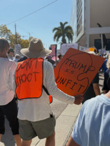 A demonstrator in a crowd wears a hi-vis vest that reads "Don't shoot" and holds a sign that reads "Trump is unfit".