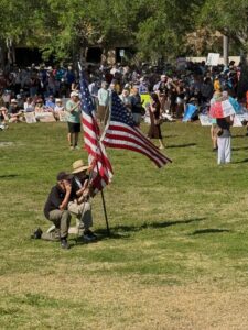 Two demonstrators hold U.S. flags in the center of a clearing. A crowd of demonstrators is in the background.