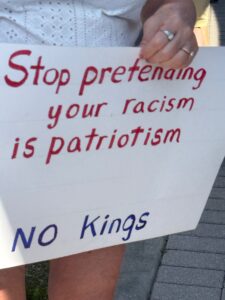 Close-up on a demonstrator's sign reading "Stop pretending your racism is patriotism. NO Kings".