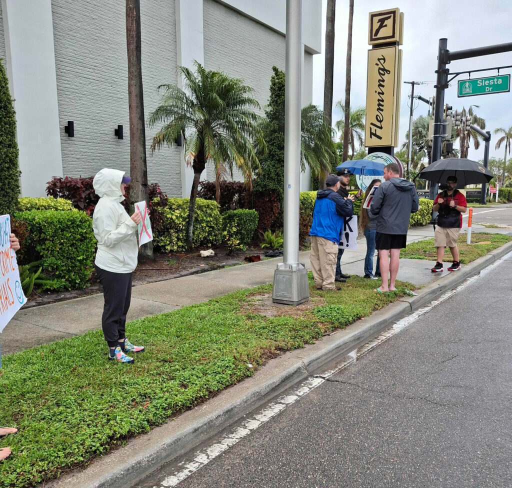 A small group of protesters holds umbrellas and signs in the rain.