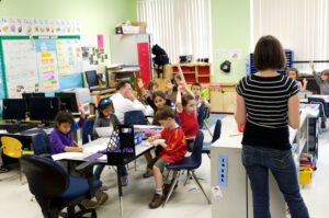 Several children raise their hands in an elementary school classroom.