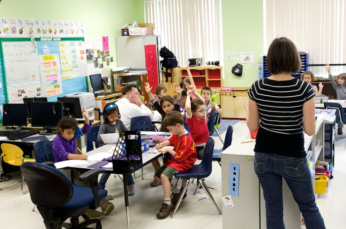 Several children raise their hands in an elementary school classroom.