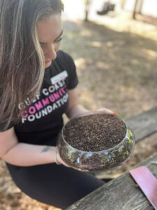 A person with a Gulf Coast Community Foundation t-shirt holding a clear bowl full of compost.