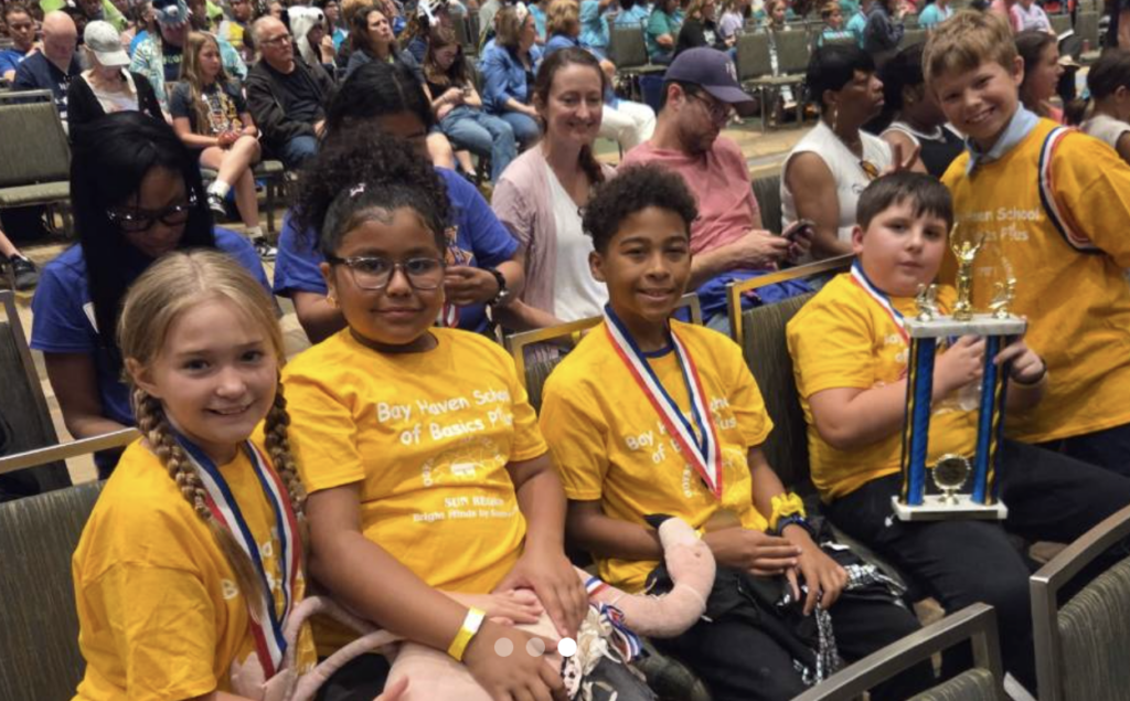 Students in yellow shirts smile for the camera and pose with a first-place trophy.