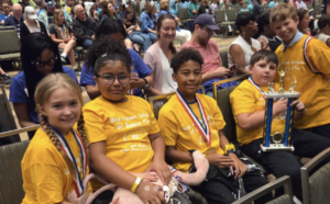 Students in yellow shirts smile for the camera and pose with a first-place trophy.