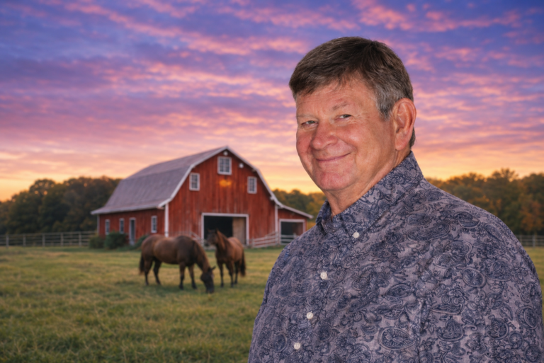 Mike Harrison smiling in front of a barn with horses at twilight.