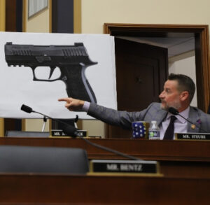 Greg Steube gesturing in front of a big presentation slide of a handgun.