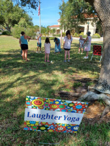 A group of seven stands in a circle outside. In the foreground, a sign advertises "Laughter Yoga".