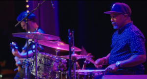 A drummer performing with a guitarist in the background at Westcoast Black Theatre Troupe