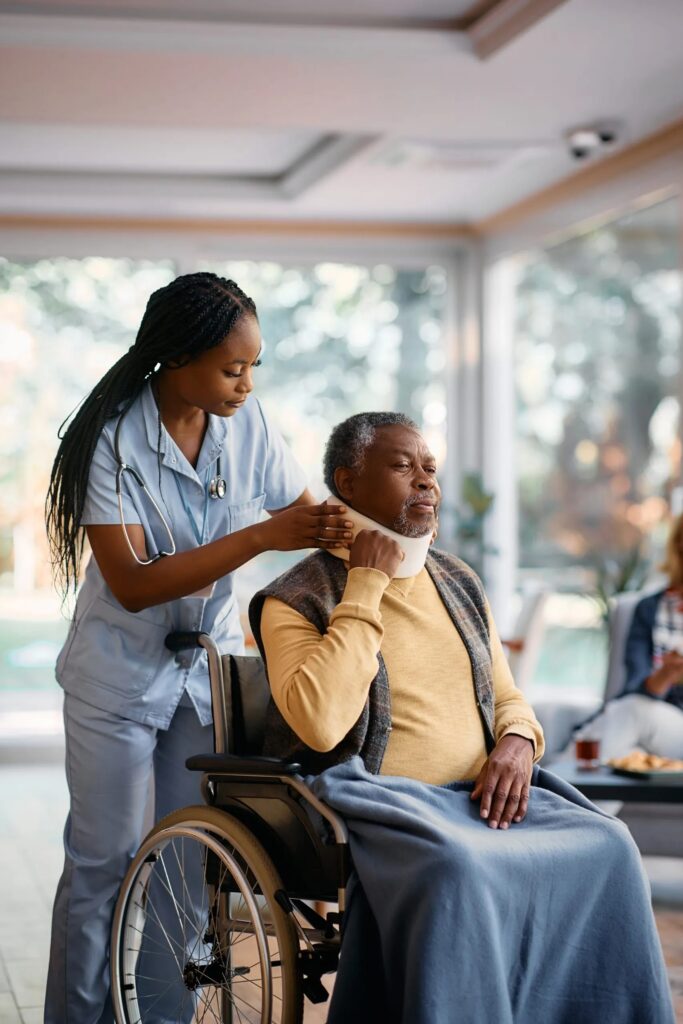 A care worker adjusting the neck brace of a patient using a wheelchair.
