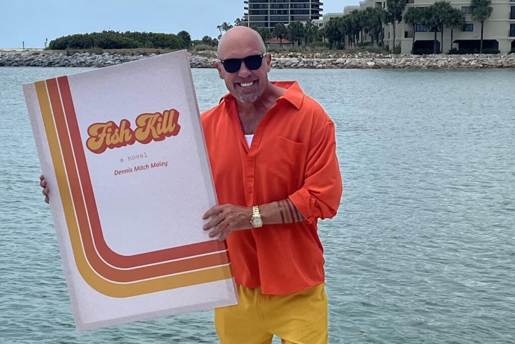 Mitch Maley smiling and holding up a huge replica cover of his novel Fish Kill.