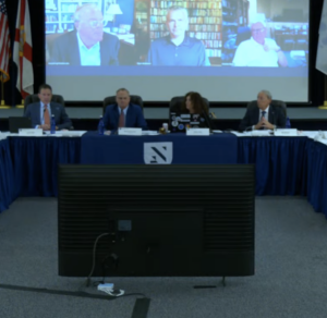 A panel of four seated at a table with New College branding. Additional people participate over Zoom.
