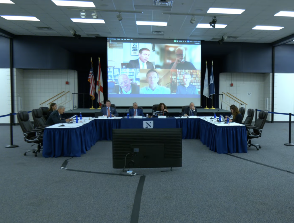 A panel of four seated at a table with New College branding. Additional people participate over Zoom.