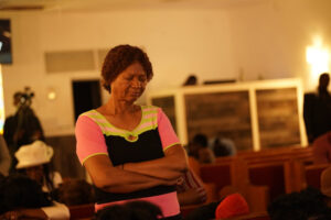 A churchgoer stands with arms folded in front of rows of pews.