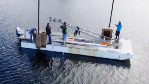 Workers stand on a pontoon boat on the water.