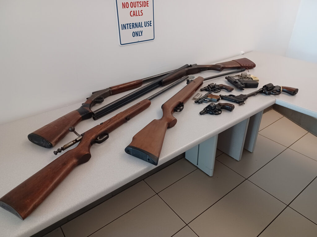 A variety of firearms strewn across a table.