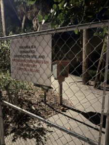 A little free library behind a chain link fence and a sign prohibiting access.
