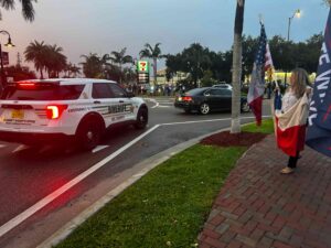 A Lee County Sheriff's vehicle next to protestors on the sidewalk carrying flags.
