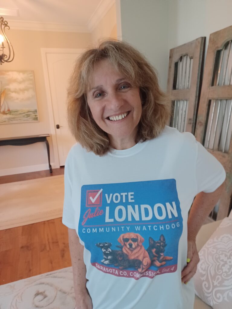 Julie London smiling and wearing a "Vote London, community watchdog" t-shirt with an illustration of three dogs wearing suglasses.