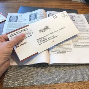 Hand holding an Oregon vote-by-mail envelope over an election guide.